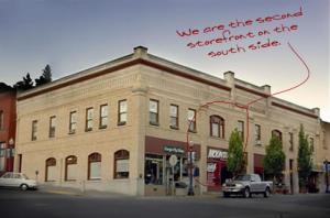 Exterior view of a historical brick building with multiple storefronts, featuring a sign that reads "We are the second storefront on the south side." The image captures the architectural details of the building and the surrounding area.