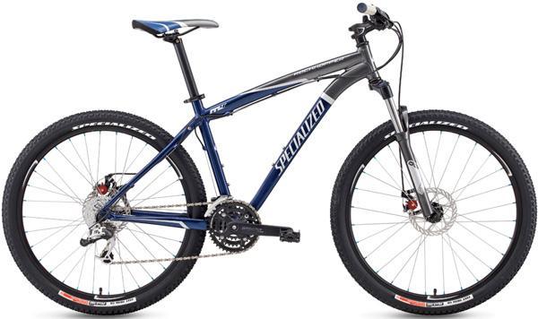 A sleek mountain bicycle with a blue and silver frame, featuring wide tires and disc brakes. The bike has a lightweight design, adjustable seat, and multiple gears for off-road cycling. The brand name "Specialized" is prominently displayed on the frame.