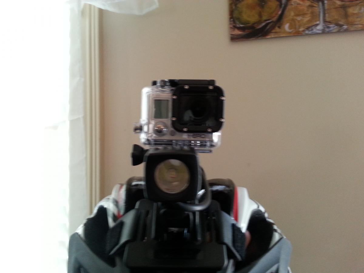 GoPro Hero3: A close-up view of a helmet with a mounted action camera on top, positioned in front of a window. A light is attached below the camera, with soft natural light illuminating the scene.