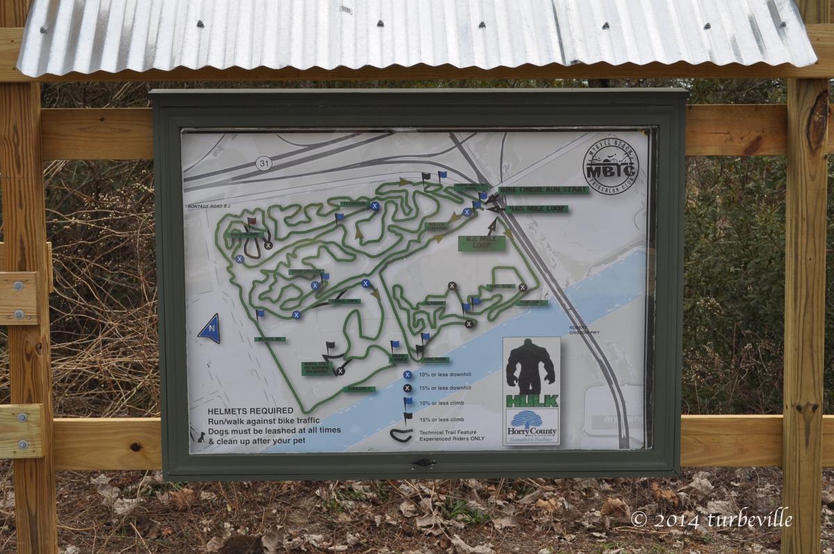 Map displaying the bike trails at a recreational area, including various loops and paths, with important information about helmet requirements, trail specifications, and rules for dog owners. Horry County Bike Run Park mountain bike trail.