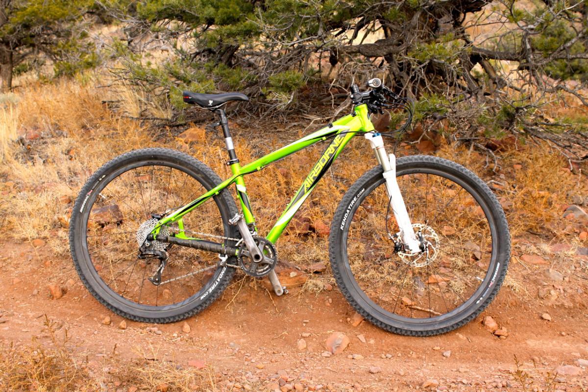 Airborne Goblin: A bright green mountain bike parked on a dirt trail surrounded by scrub and rocky terrain, with a focus on its BMX-style frame and sturdy tires.