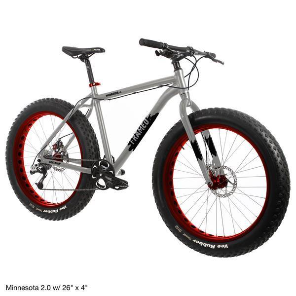 Framed Minnesota 2.0: A silver fat bike with large 26-inch tires featuring red rims. The bike has a rugged frame, black handlebars, and a disc brake system. It is designed for off-road cycling and winter conditions.