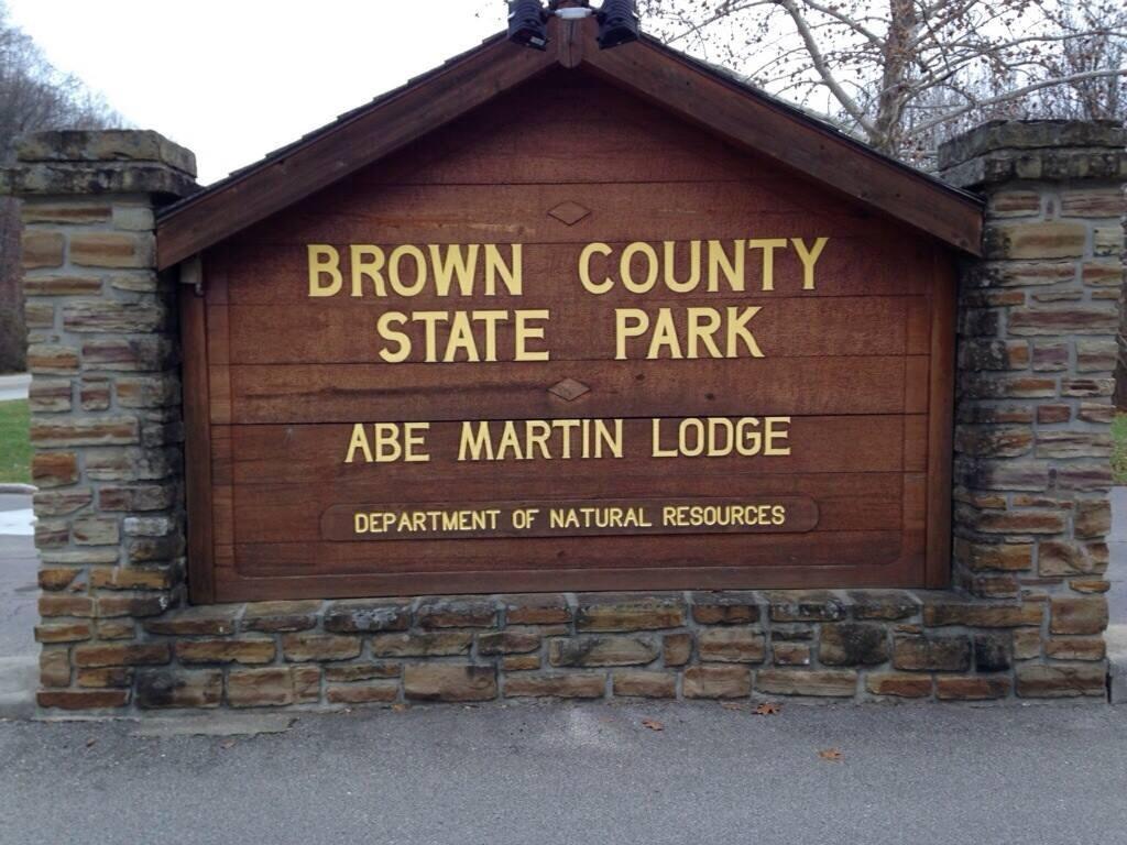 Sign for Brown County State Park, featuring "Abe Martin Lodge" and "Department of Natural Resources." The sign has a wooden background with golden lettering and is surrounded by stone pillars. Brown County Park mountain bike trail.