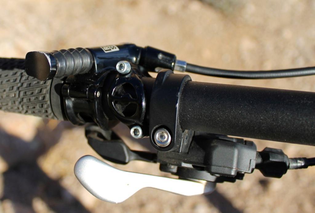 GT Force Carbon Pro: Close-up view of a bicycle handlebar with a gear shift lever, brake lever, and textured grip, set against a blurred outdoor background.