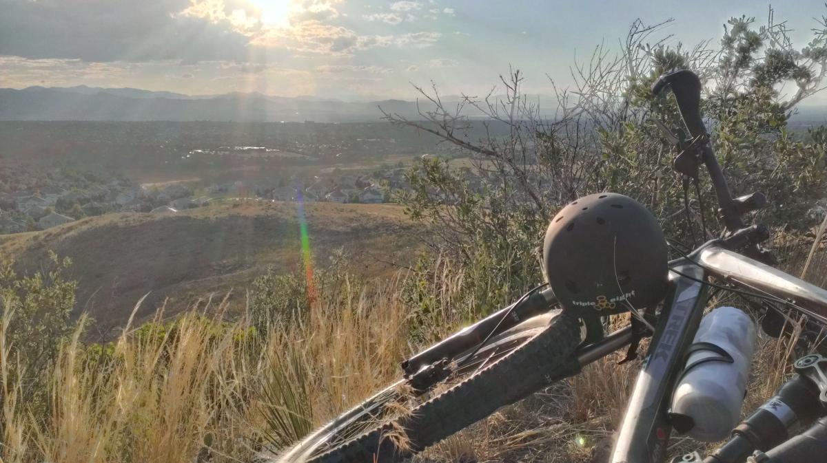 Trek Fuel EX 8: A mountain bike resting on grass with a helmet and water bottle beside it, overlooking a valley with sunlight shining through the clouds in the background.