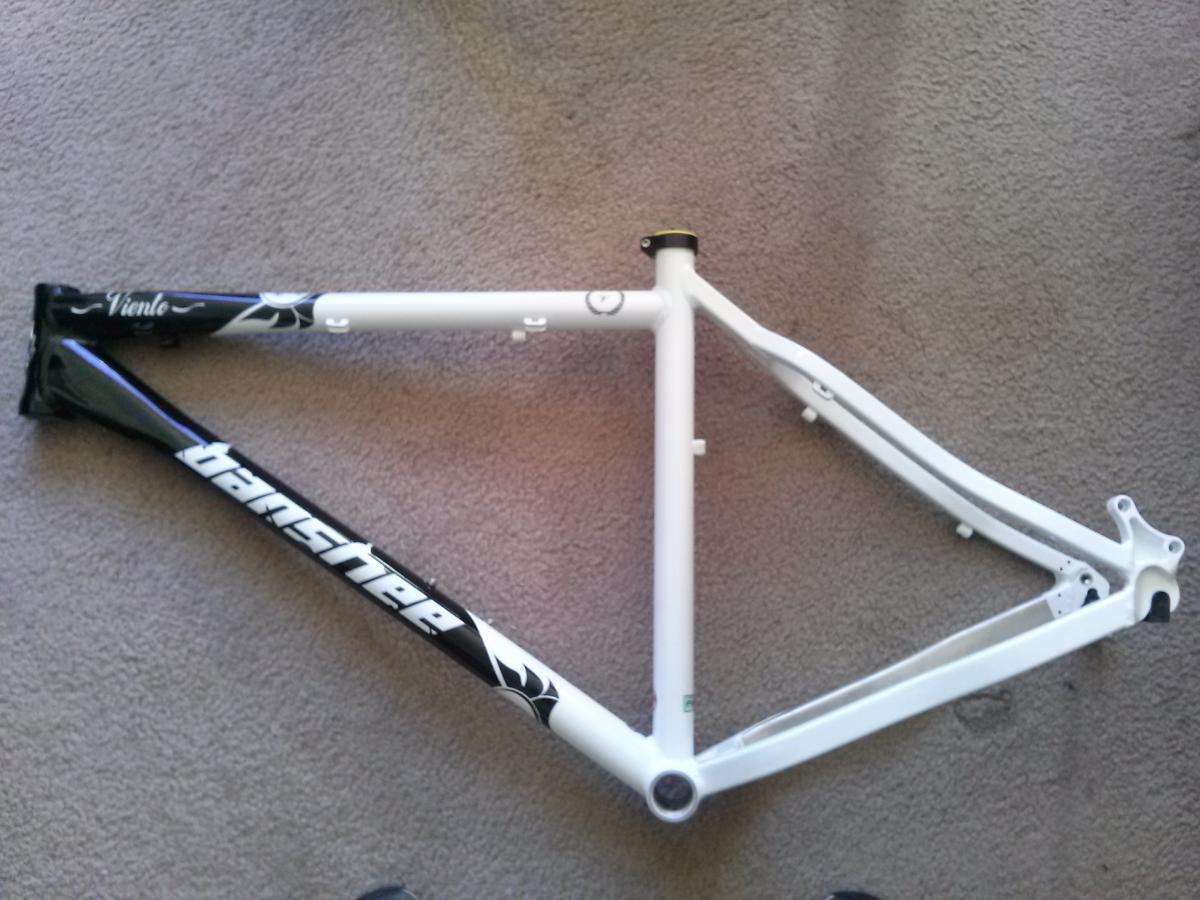 Banshee Viento: A bicycle frame laid out flat on a carpeted surface, featuring a combination of black and white colors. The frame is marked with the brand name "Banshee" in white lettering and includes additional graphics on the top tube.
