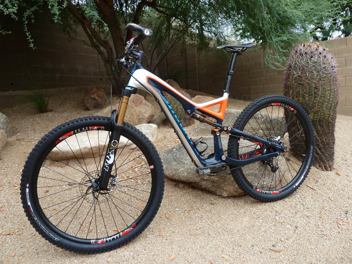 Specialized SWORKS Stumpjumper FSR: Mountain bike parked on rocky terrain surrounded by desert vegetation, featuring a blue and orange frame, black wheels, and a cactus in the background.