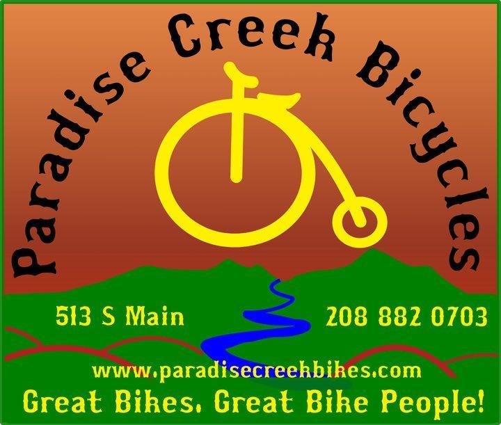 A colorful logo for Paradise Creek Bicycles featuring a stylized bicycle icon in yellow on a gradient brown and green background. The text includes "Paradise Creek Bicycles," address "513 S Main," phone number "208 882 0703," and the website "www.paradisecreekbikes.com." The tagline reads, "Great Bikes. Great Bike People!"