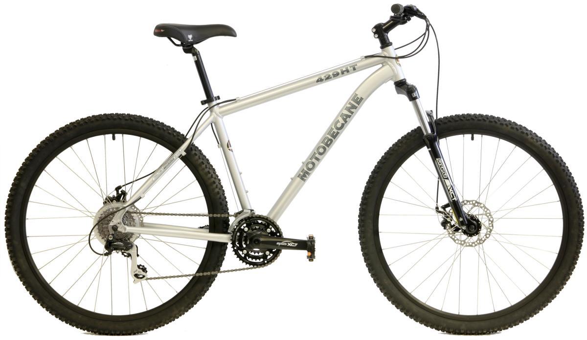 Motobecane 429HT: Alt text: A silver Motobecane 429HT mountain bike featuring thick, knobby tires, a front suspension fork, and a multi-speed gear system. The bike is positioned to show its frame design and components.