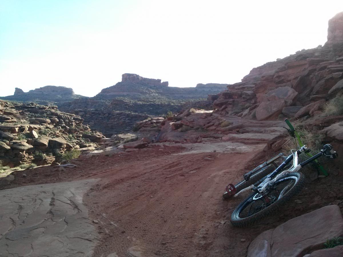 A mountain bike lying on a dirt trail, surrounded by rocky terrain and distant mountains under a clear sky. The scene captures a serene outdoor setting ideal for biking and exploration. Amasa Back Trail mountain bike trail.