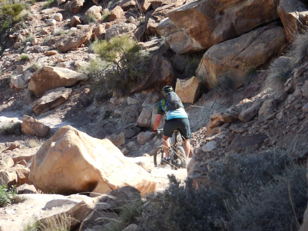 A mountain biker navigating a rocky trail surrounded by large boulders and sparse vegetation in a rugged outdoor setting. Sovereign Single Track mountain bike trail.