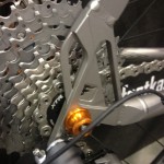 Close-up view of the rear derailleur and cassette of a bicycle, showcasing a silver and orange component, with a focus on the gear mechanism and chain.