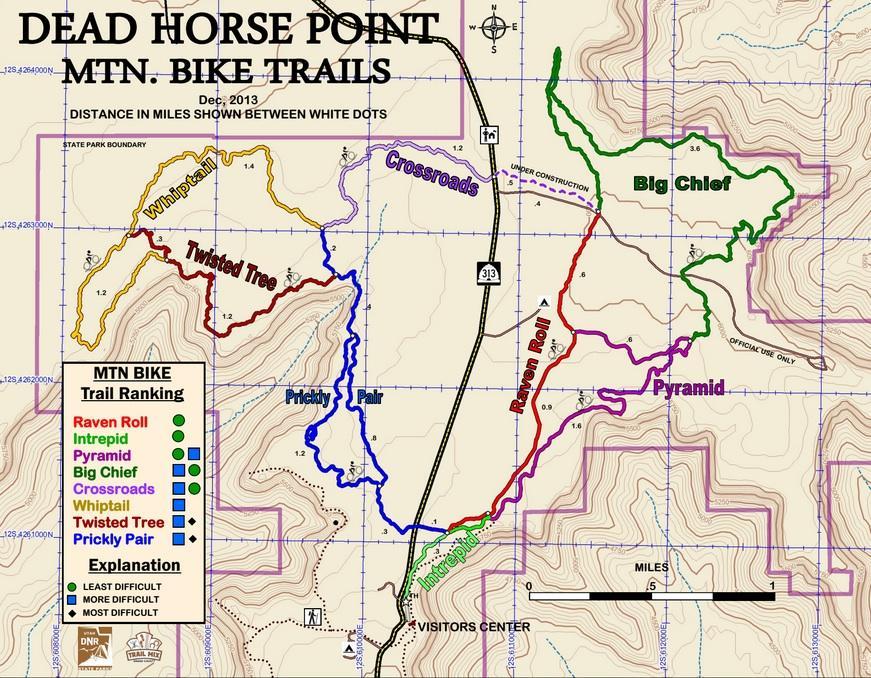 Map of Dead Horse Point Mountain Bike Trails, December 2013. The map shows various biking trails including Raven Roll, Intrepid, Pyramid, Big Chief, Crossroads, Whiptail, Twisted Tree, and Prickly Pair, with distances indicated between white dots. Trails are color-coded to represent different difficulty levels, with a legend provided. The visitors center is marked, along with a scale bar for distance measurement. Dead Horse Point State Park mountain bike trail.