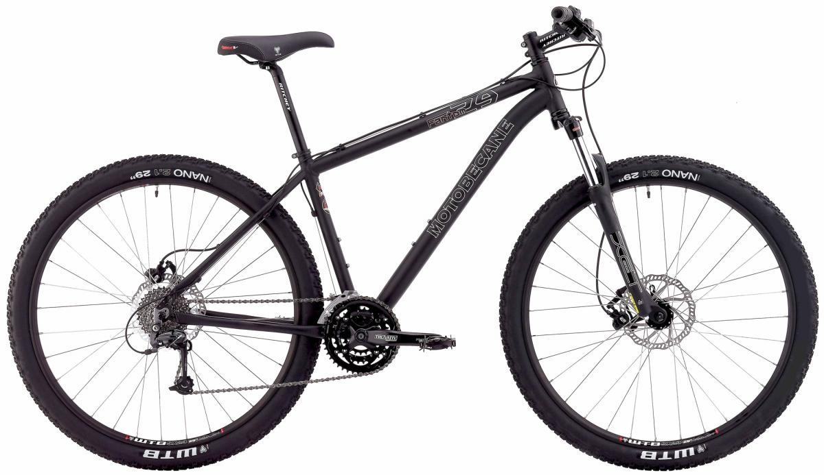 Motobecane Fantom 29: A black mountain bike with a sturdy frame, large tires, and a gear system, featuring disc brakes and handlebars. The bike is positioned upright against a plain background, showcasing its design and components.