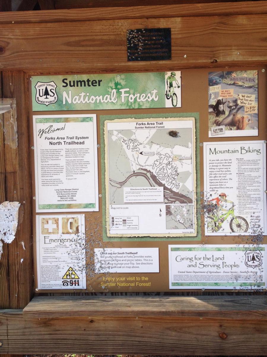 Information display board for the Forks Area Trail System in the Sumter National Forest. The board includes a welcome message, trail maps, emergency information, and guidelines for mountain biking. It features images related to biking and nature conservation, as well as details on trail access and a reminder to enjoy the Forest. Forks Area Trail System (FATS) mountain bike trail.