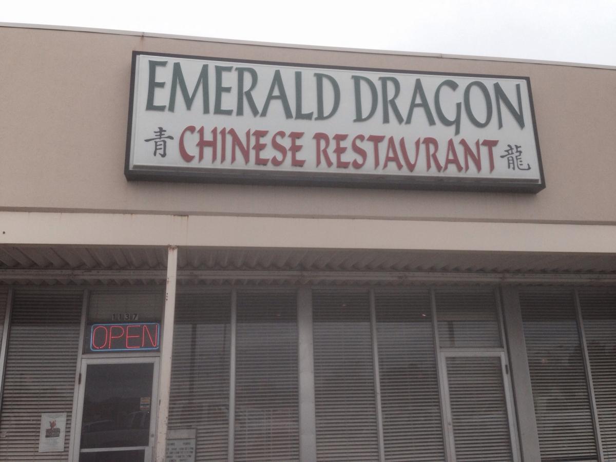 Signage for the Emerald Dragon Chinese Restaurant, displaying the name in bold letters. The restaurant is open, as indicated by a neon "OPEN" sign in the window. The building features a simple storefront design with slatted windows. Spadra Creek Nature Trail mountain bike trail.