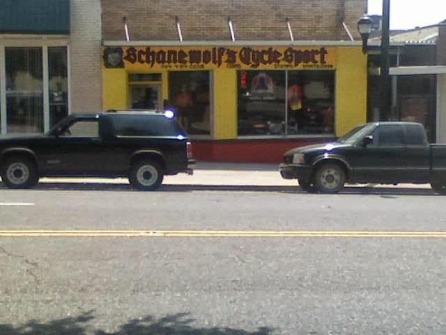 Black SUVs parked on a street in front of a storefront with a yellow sign reading "Schanewolf