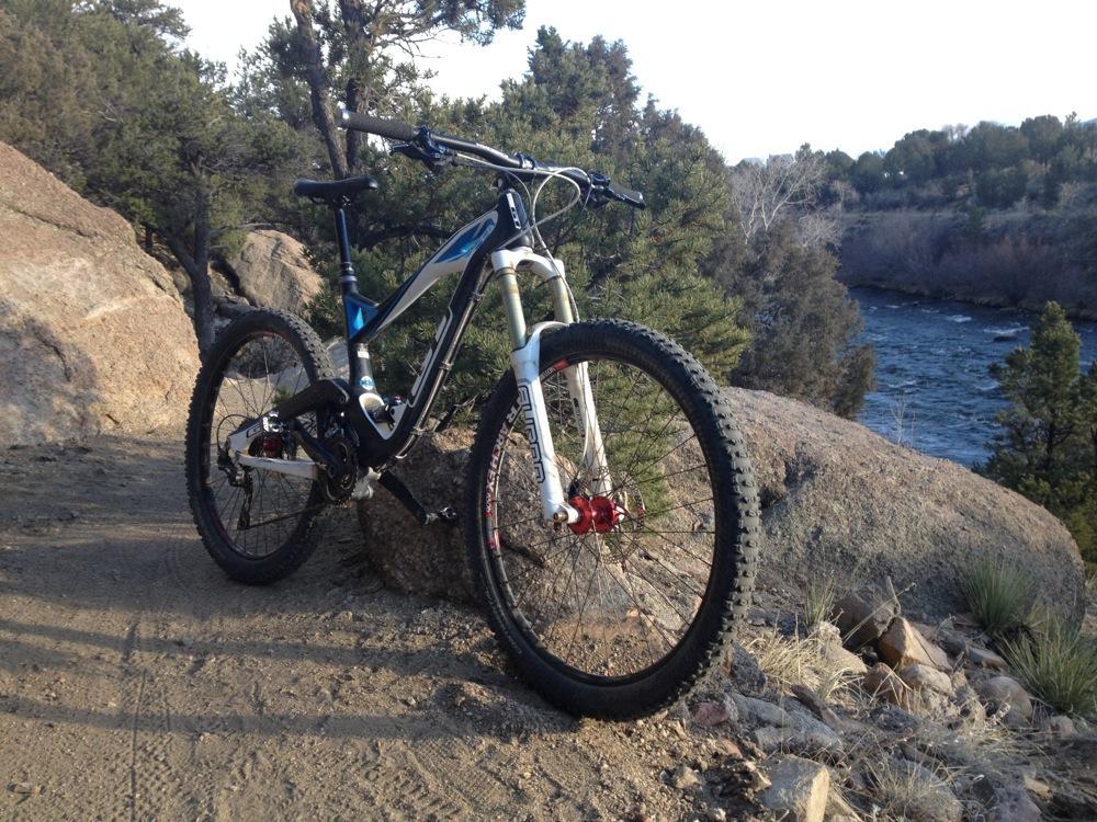 GT Force Carbon Pro: Mountain bike resting on a large rock beside a river, with trees in the background and a sandy path in the foreground.