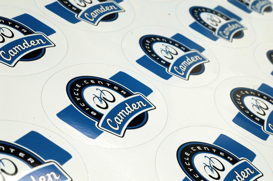 A collection of round stickers featuring the logo of the Camden Bicycle Center. The logo is primarily black and blue, with the words "Bicycle Center" and "Camden" prominently displayed. The stickers are arranged in a repeated pattern on a white background.