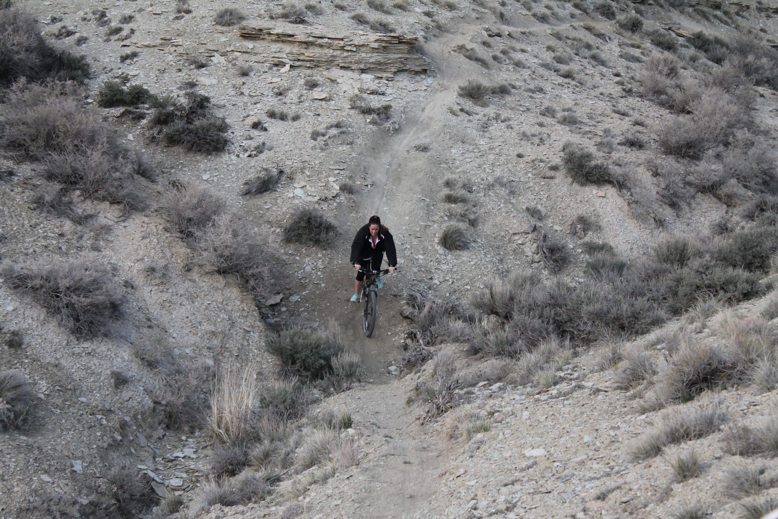 A person riding a mountain bike on a rocky trail surrounded by sparse vegetation and rocky terrain, showcasing an outdoor adventure in a rugged landscape. Uncle Ricos mountain bike trail.