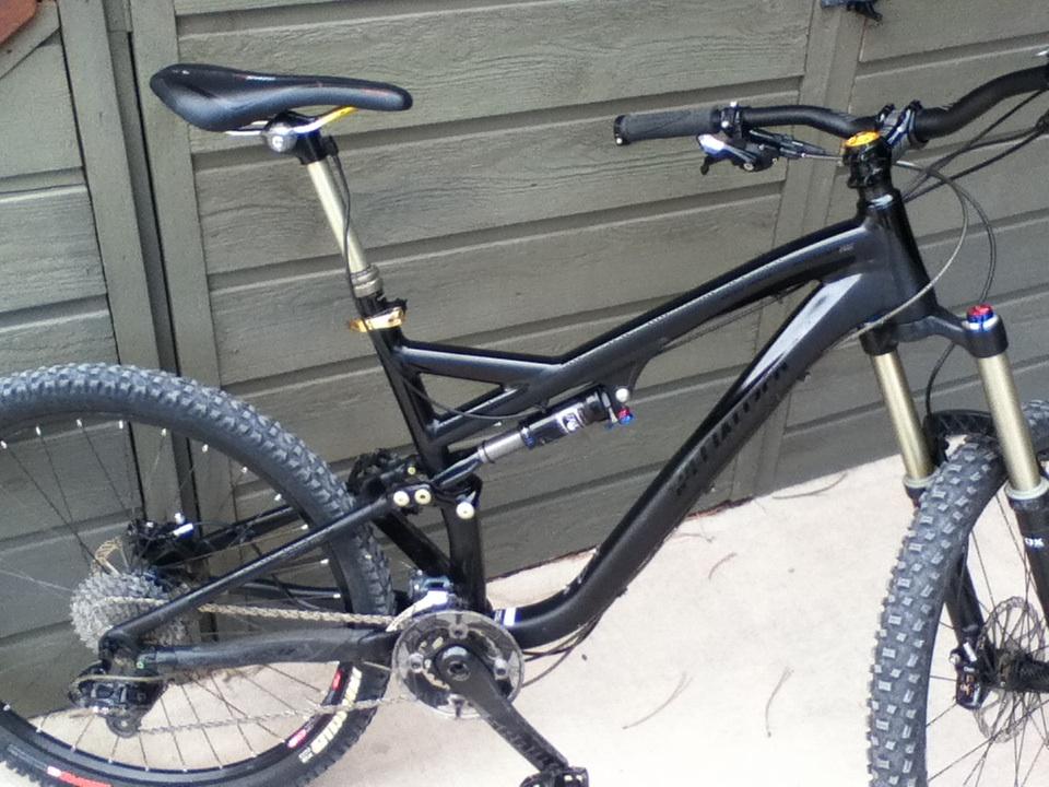 Specialized Stumpjumper FSR Expert Evo: A black mountain bike with distinctive suspension features, showcasing its frame, handlebars, and wheels. The bike is positioned against a rustic wooden backdrop, highlighting its rugged design and off-road capabilities.