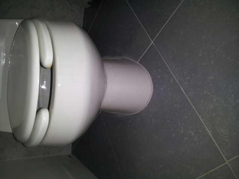 A close-up view of a white toilet on gray tiled flooring, taken from an angle that highlights the toilet's bowl and seat.