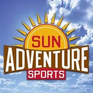 Logo for "Sun Adventure Sports," featuring a stylized sun with rays and the text "Adventure Sports" prominently displayed beneath it, set against a background of blue sky and clouds.