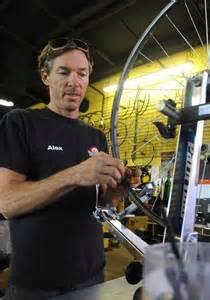 A bicycle mechanic working on a bike wheel in a workshop, focused on adjusting components, with bicycles visible in the background.
