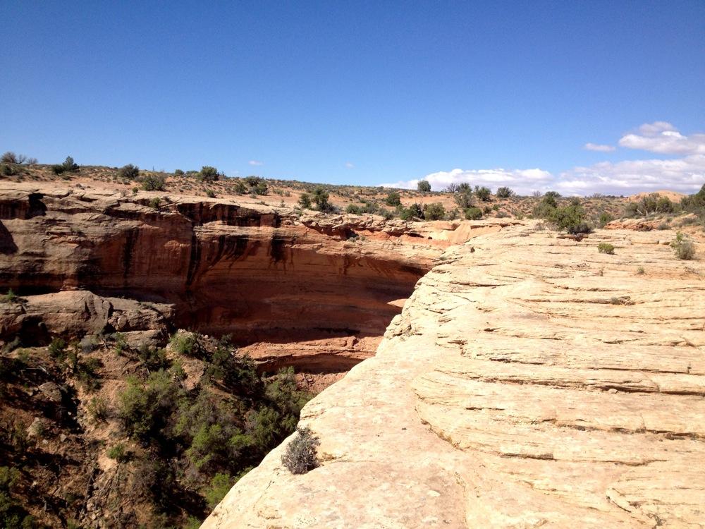 A panoramic view of a rocky canyon landscape under a clear blue sky, featuring layered stone formations and sparse vegetation. The scene captures the rugged terrain and natural beauty of the area, with cliffs and a distant horizon visible in the background. Rocky Tops mountain bike trail.