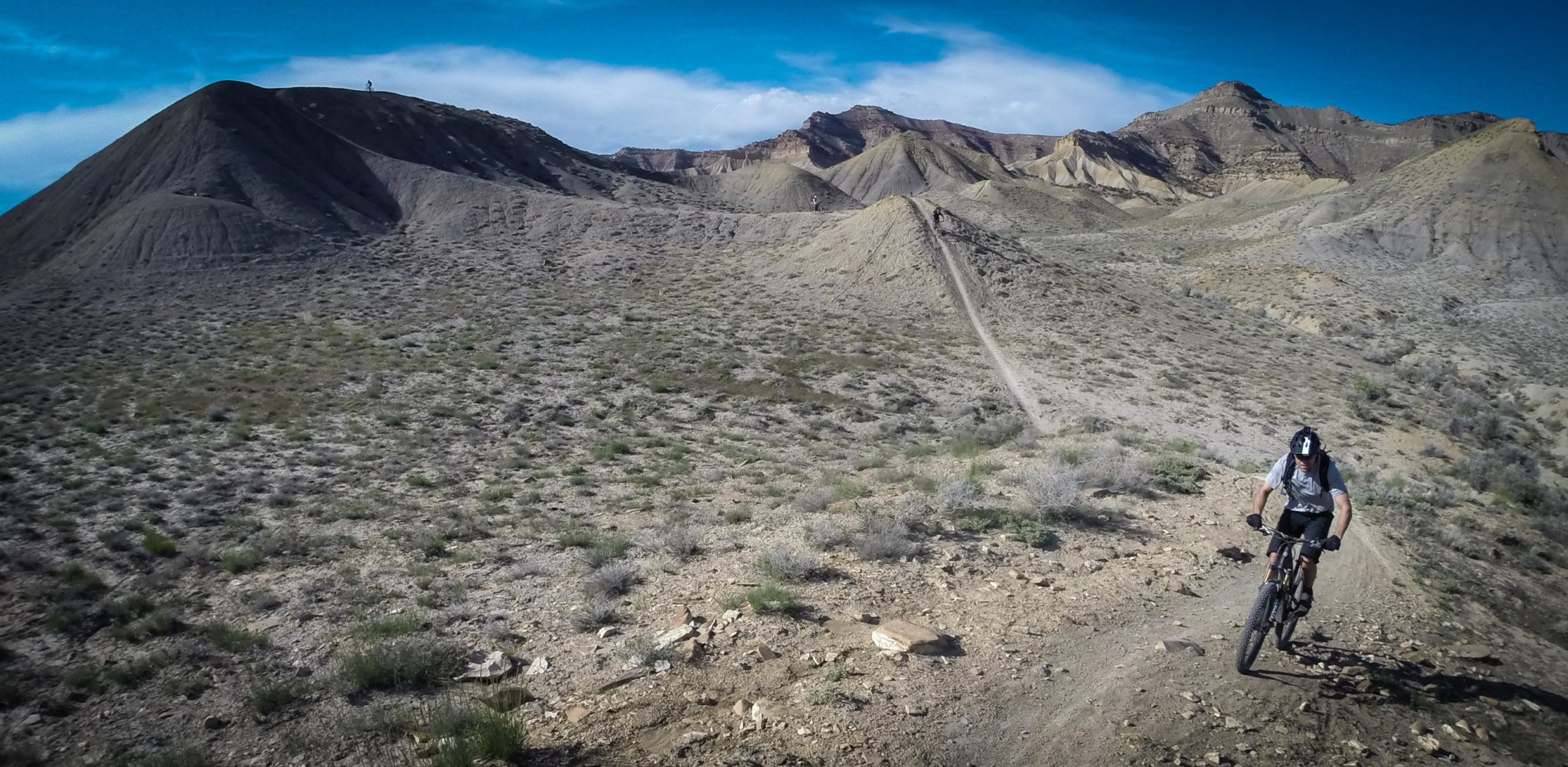 A mountain biker navigating a rocky trail in a desert landscape, surrounded by distant hills and a clear blue sky. The terrain features sparse vegetation and rugged terrain, highlighting the challenging environment for biking. Zippety Do Dah mountain bike trail.