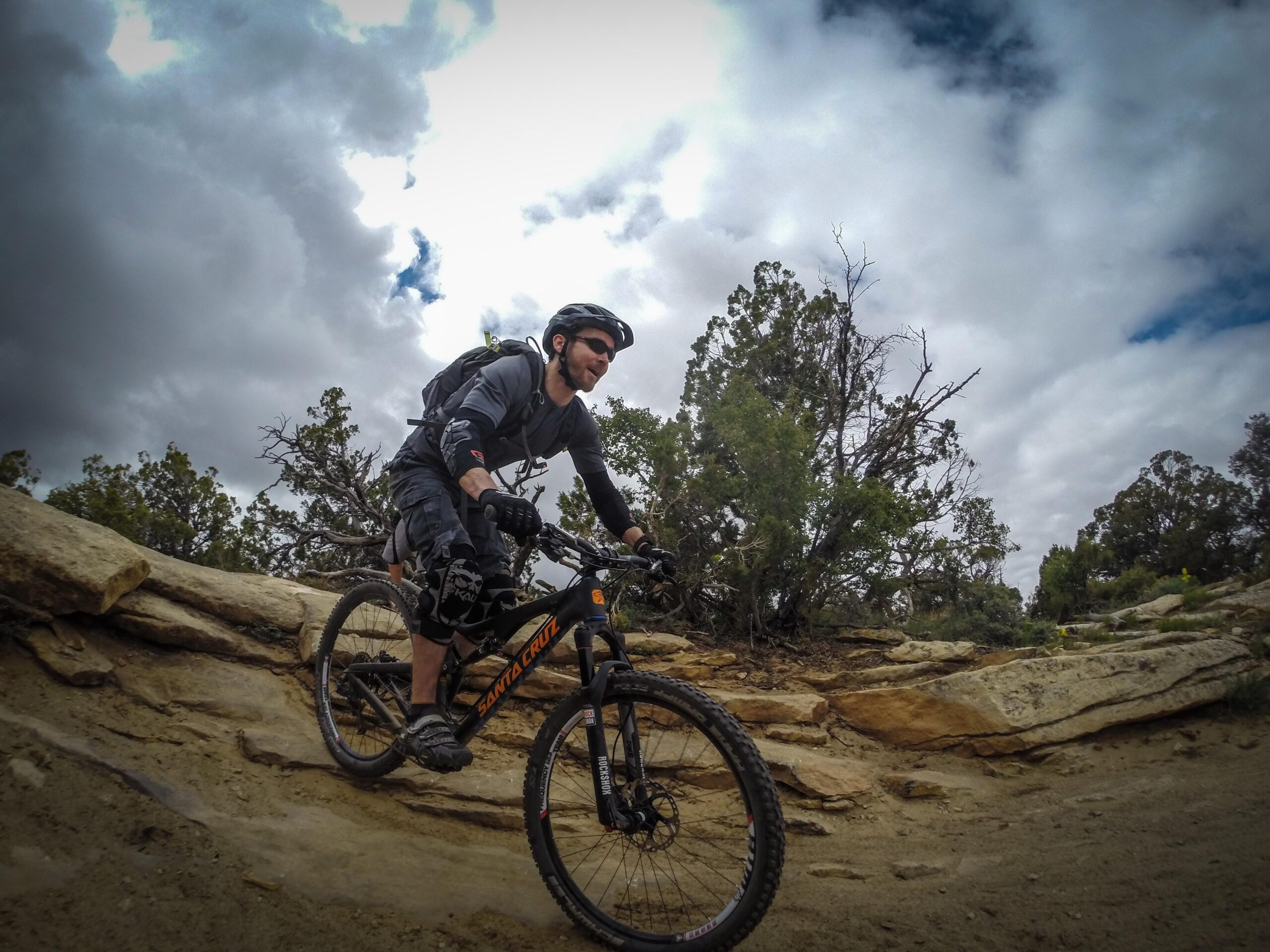 A mountain biker navigating a rocky trail under a cloudy sky, surrounded by sparse vegetation and rugged terrain. The rider is wearing a helmet and protective gear, showcasing an adventurous spirit in an outdoor setting. Porcupine Rim mountain bike trail.