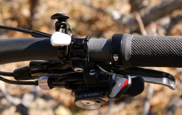 Rocky Mountain Instinct 999 MSL: Close-up view of a bicycle handlebar featuring gear shift controls, a textured grip, and a lever. The background shows a blurred, natural outdoor setting.