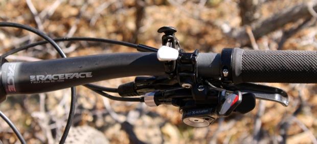 Rocky Mountain Instinct 999 MSL: Close-up view of a bicycle handlebar featuring a Race Face grip, a brake lever, and a gear shifter. The background is natural and slightly blurred, suggesting an outdoor setting.