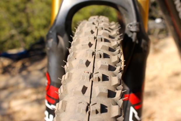 Rocky Mountain Instinct 999 MSL: Close-up view of a mountain bike tire showing its tread pattern, with the focus on the rubber texture and detail. The tire is partially visible alongside the bike frame, with a blurred background of natural terrain. Dust and dirt indicate the tire has been used on outdoor trails.