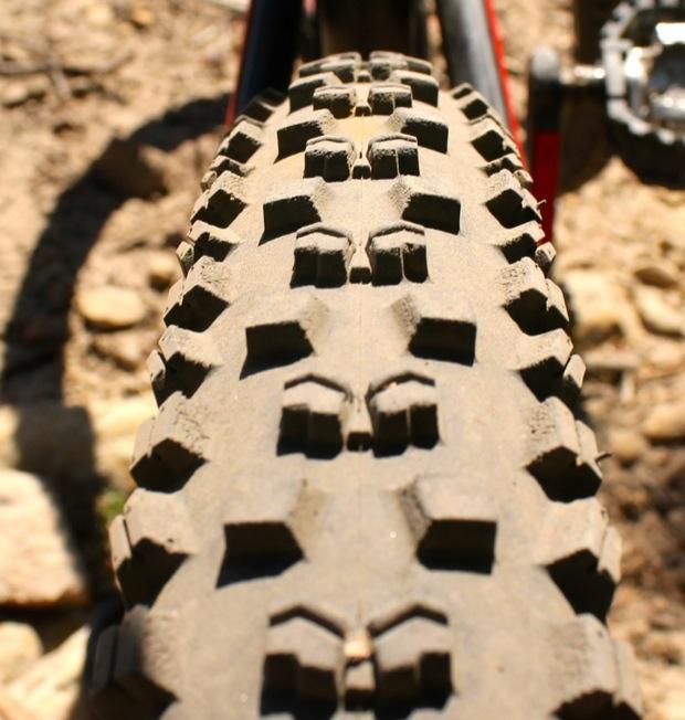 Rocky Mountain Instinct 999 MSL: Close-up view of a mountain bike tire showing a rugged tread pattern, designed for traction on uneven terrain, with dirt and small rocks in the background.
