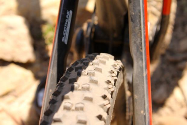 Rocky Mountain Instinct 999 MSL: Close-up view of a rugged mountain bike tire, showcasing its textured tread pattern, with the bike frame partially visible in the background. The tire appears slightly dirty, indicating use on rough terrain.