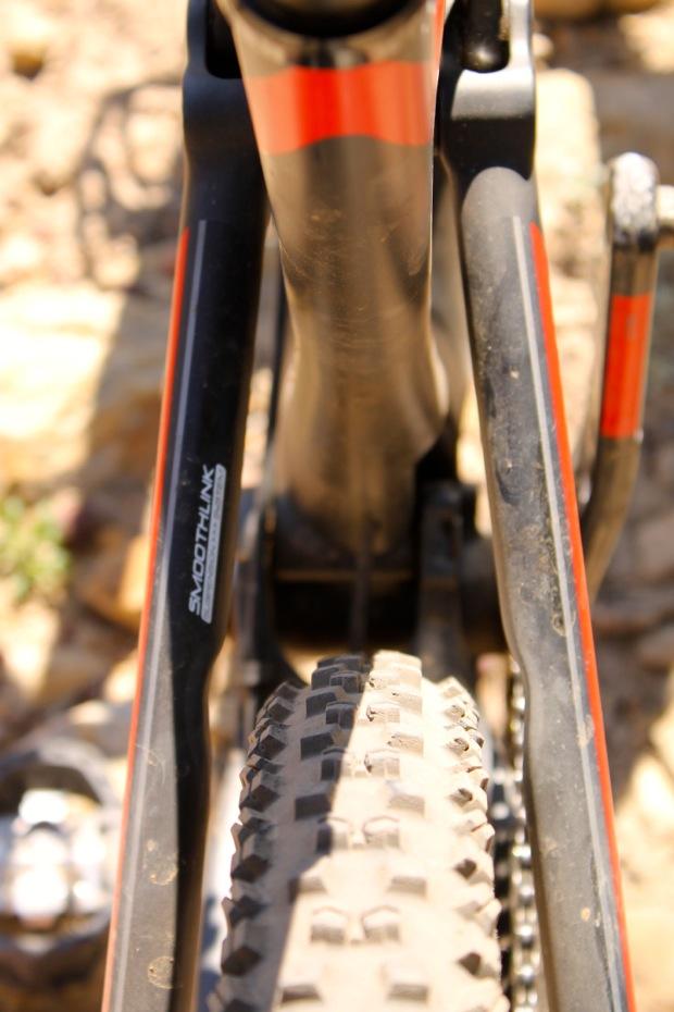 Rocky Mountain Instinct 999 MSL: Close-up view of a bicycle frame with a focus on the rear wheel and tire. The frame is black with orange accents, and some components are visible in the background. The tire has a textured tread pattern, indicating it is designed for off-road or mountain biking conditions.