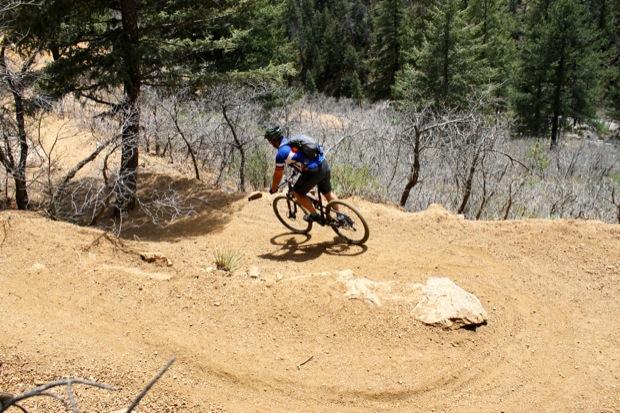 Rocky Mountain Instinct 999 MSL: A mountain biker navigating a winding dirt trail surrounded by trees, demonstrating agility on a sunny day.
