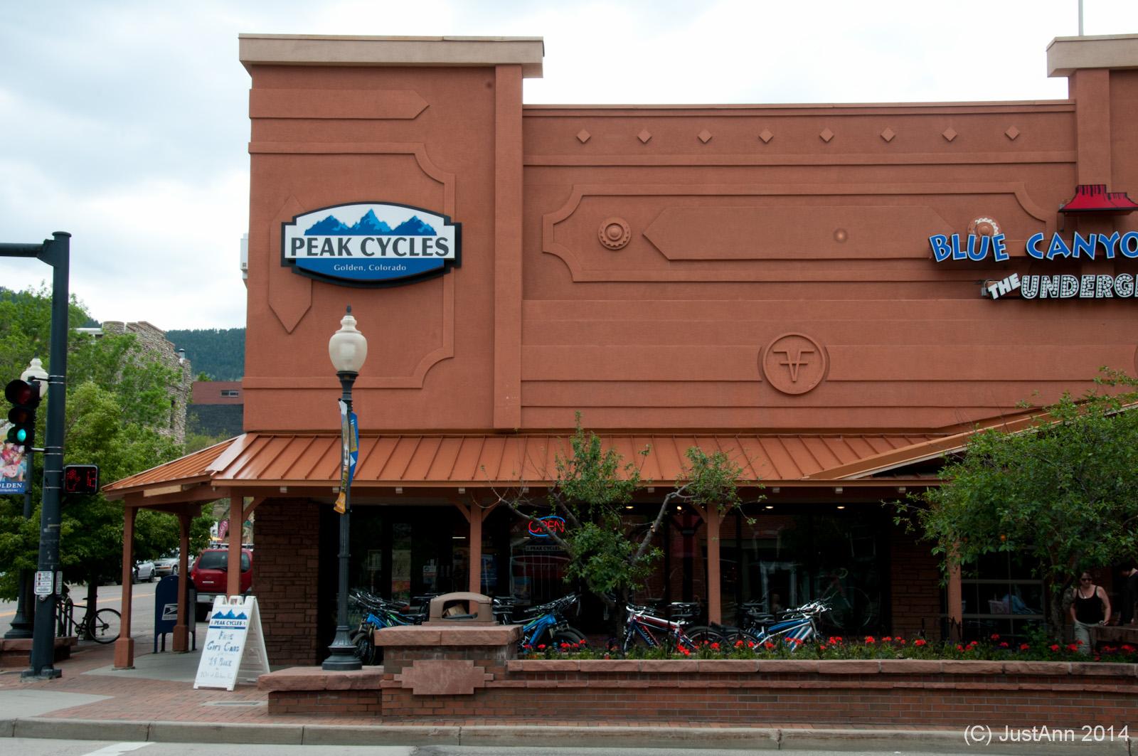 A storefront view of Peak Cycles in Golden, Colorado, featuring a prominent sign with the shop