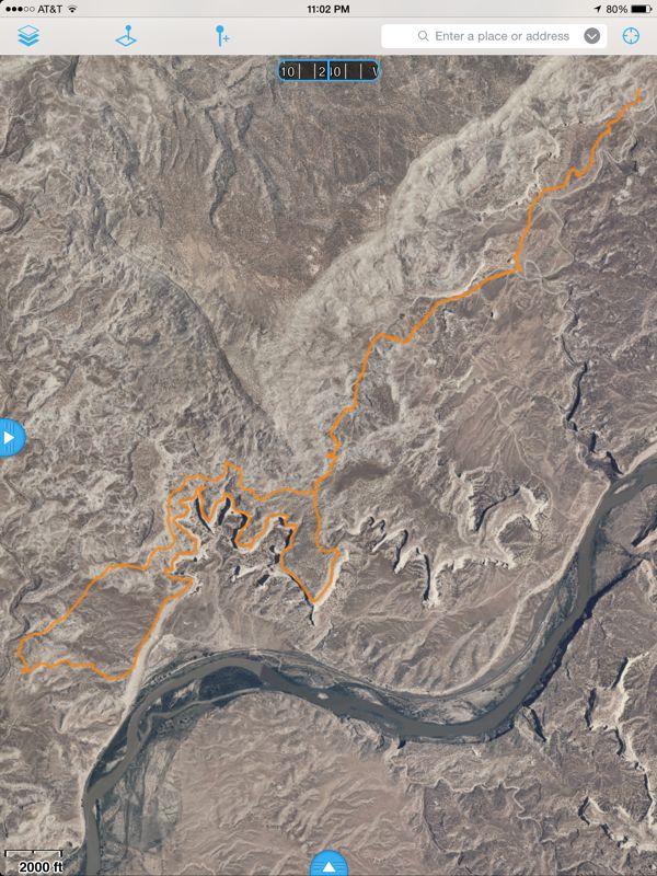 Aerial view of a rugged landscape featuring winding terrain and a river. An orange path marks a specific route through the dry, mountainous region, showcasing natural features like hills and valleys. The scale indicates the distance, with measurements shown in feet. Western Rim mountain bike trail.