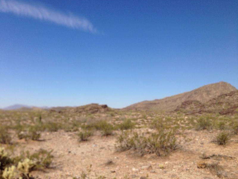 A blurred image of a desert landscape featuring rolling hills, sparse vegetation, and a clear blue sky. Desert Classic mountain bike trail.