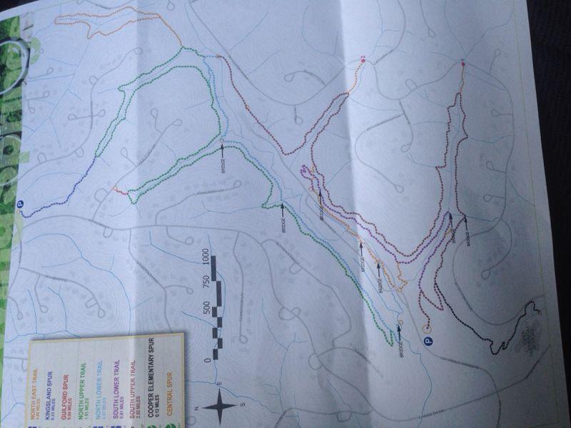 A detailed trail map featuring various colored paths indicating different hiking or biking routes. The map includes labeled features such as trail names, elevation markers, and a legend for trail difficulty levels. It also has directional arrows to guide users through the landscape. The background displays a topographical design with contour lines. Blowing Springs mountain bike trail.