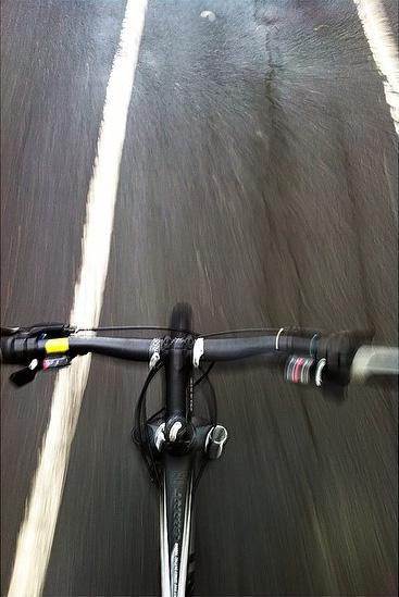 Giant Revel 29er: A close-up view of a bicycle's handlebars while riding along a blurred asphalt path, with visible white bike lane markings and a sense of motion.