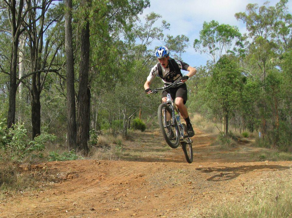 Giant Anthem 2: A mountain biker in mid-air performing a jump on a dirt trail surrounded by trees and greenery.
