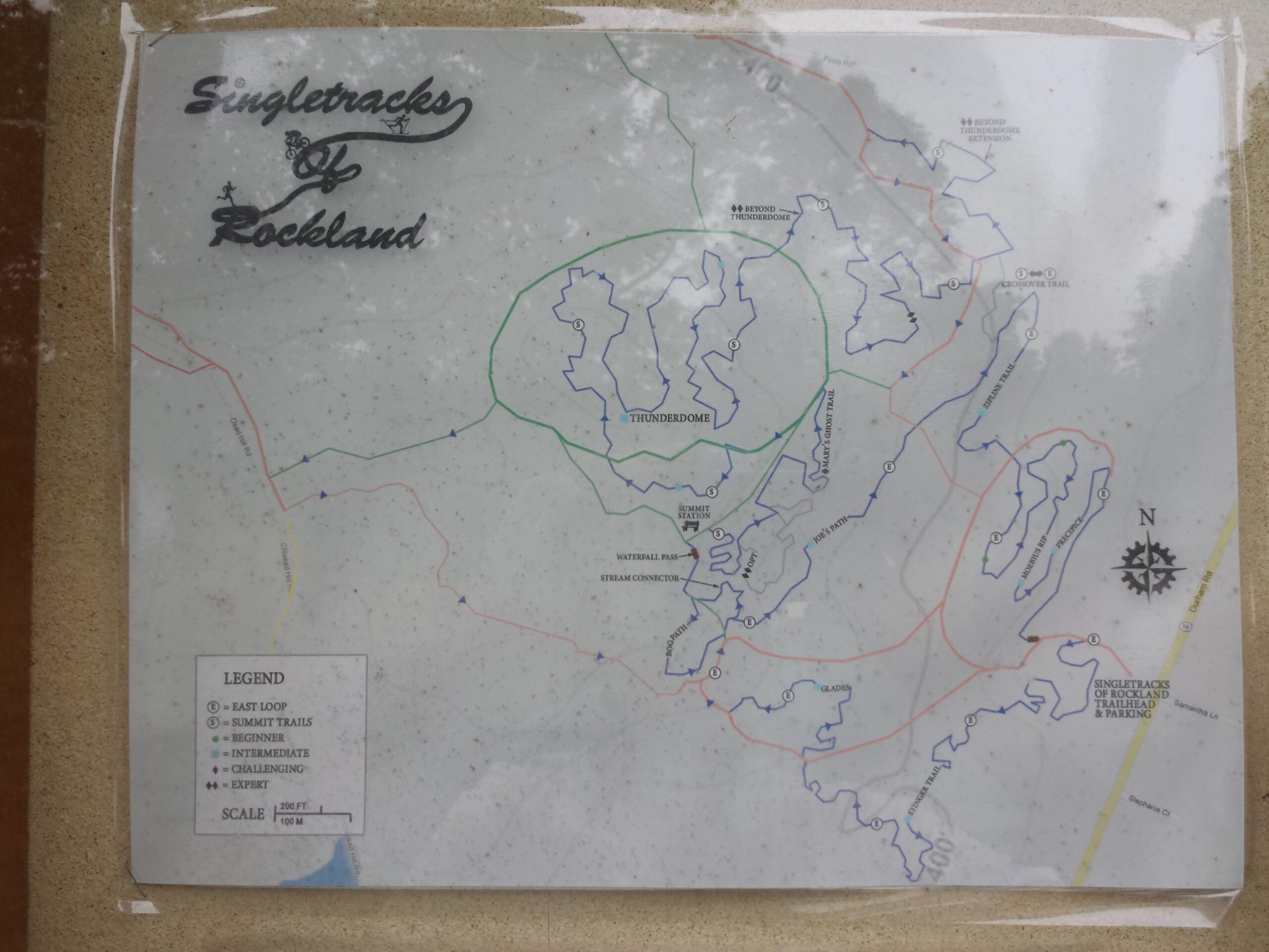 Map of the Singletracks of Rockland, showing trail routes and difficulty levels. The legend indicates various trail types: East Loop (circle), Summit Trails (triangle), and levels for beginner, intermediate, challenging, and expert trails. The map includes a north indicator and a scale. Rockland Preserve mountain bike trail.
