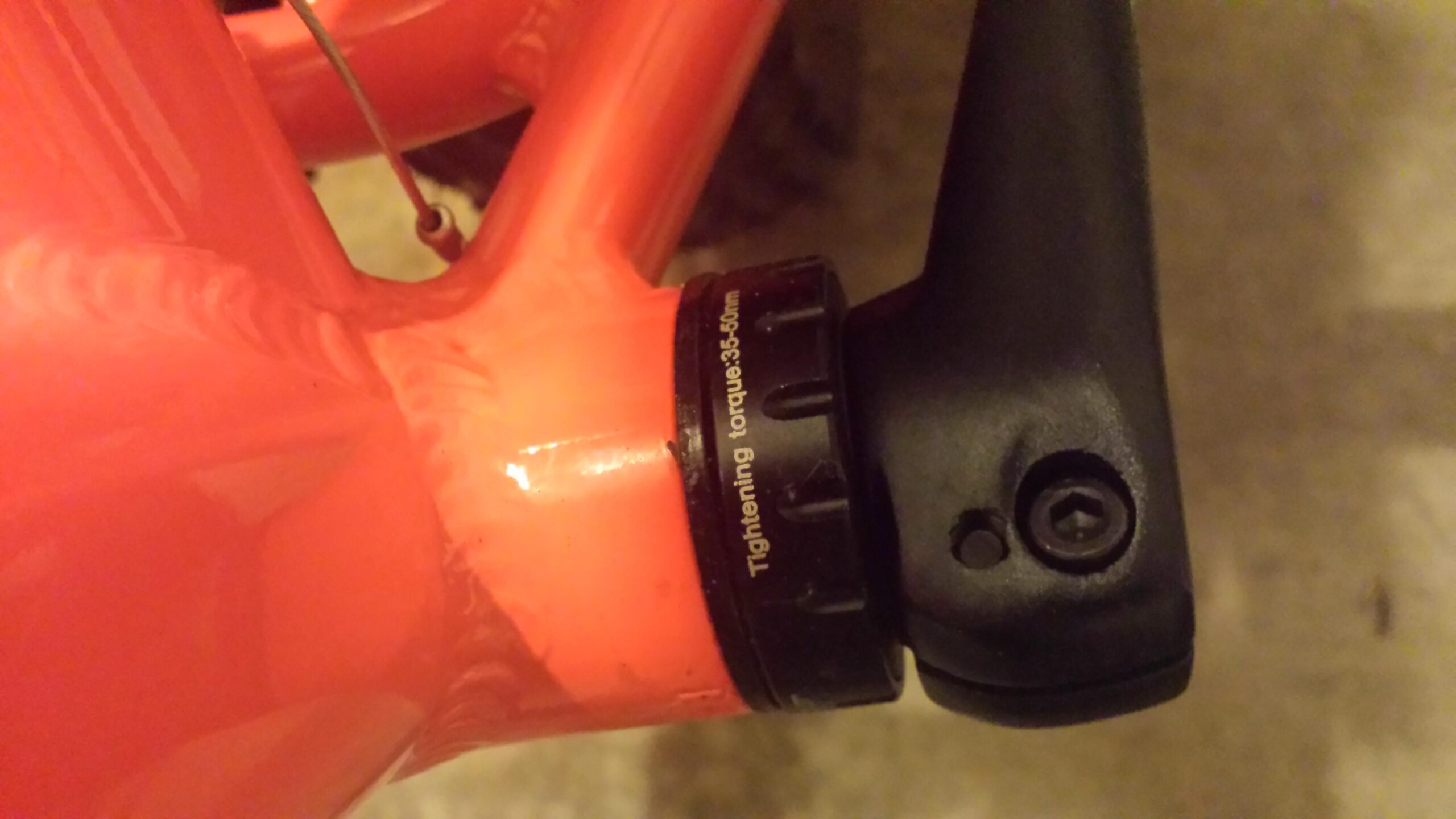 Motobecane FB4 Comp: Close-up view of a bicycle's bottom bracket area, featuring a brightly colored orange frame and a black component labeled "Tightening torque 35-50 Nm." The image highlights the connection between the frame and the black part, which appears to be part of the bike’s drivetrain setup.
