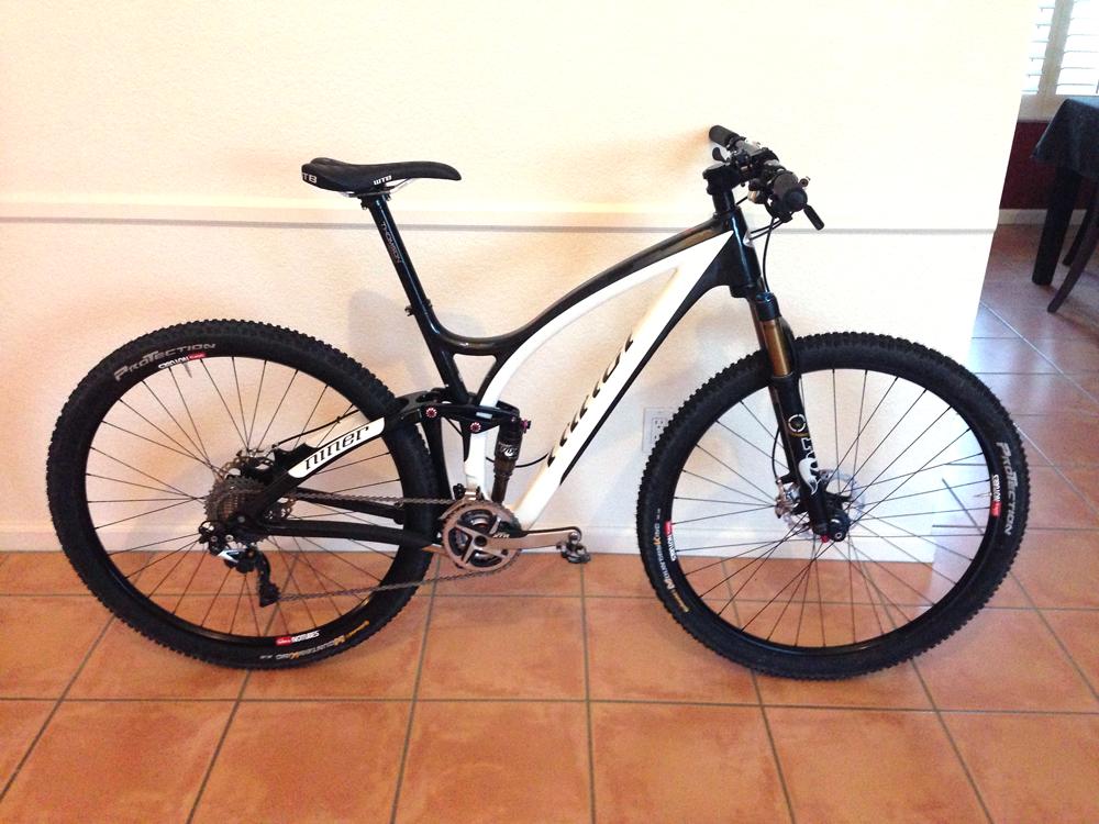 Niner Jet 9 RDO: A black and white mountain bike leaning against a wall, showcasing its sleek frame and high-performance components. The bike features thick tires, disc brakes, and a suspension fork, set on a tiled floor in an indoor setting.