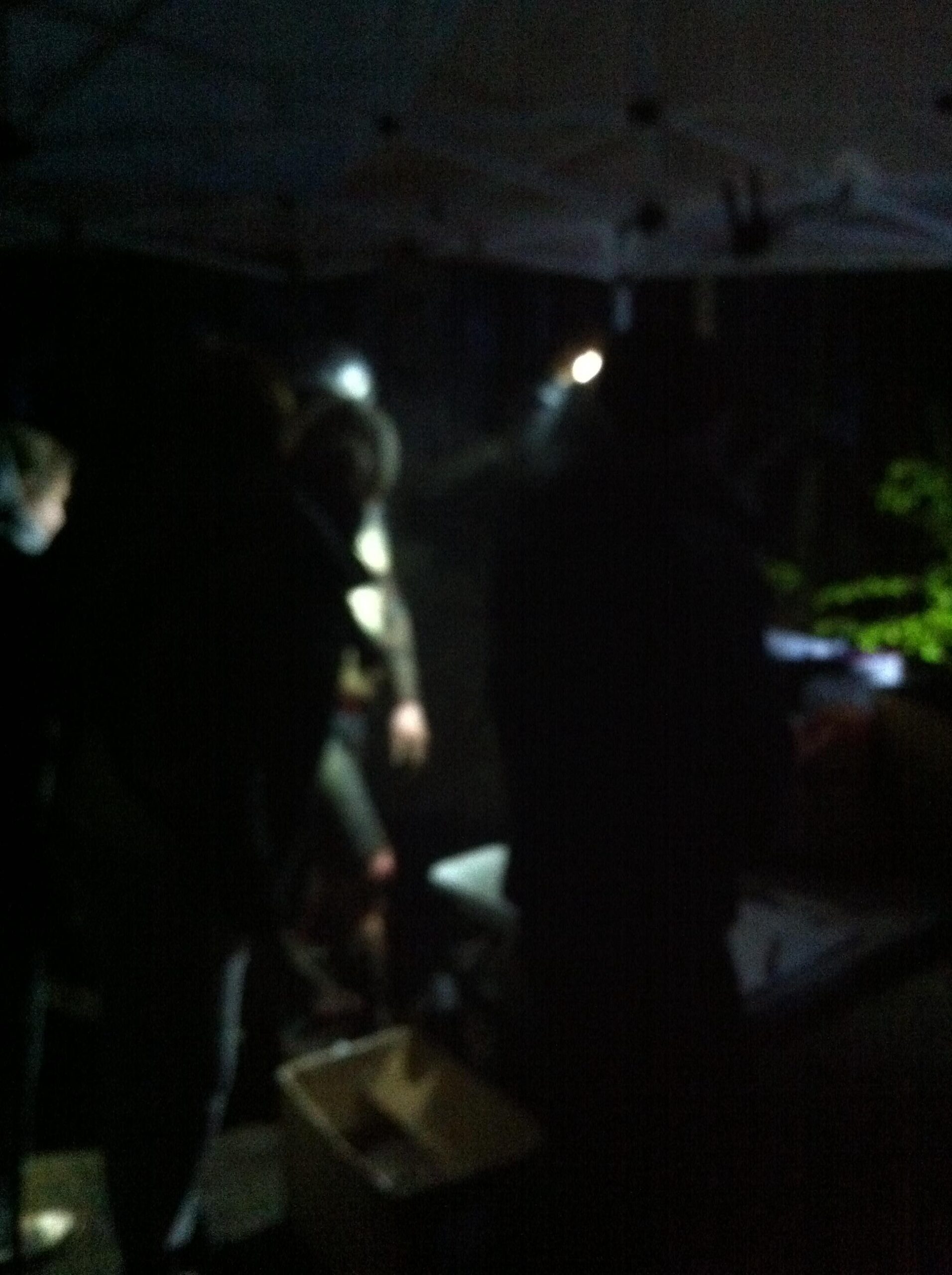 Specialized Camber: A dimly lit scene showing a group of people gathered under a tent at night, illuminated by flashlights. The figures are partially obscured, creating a sense of activity and engagement in a dark outdoor environment.