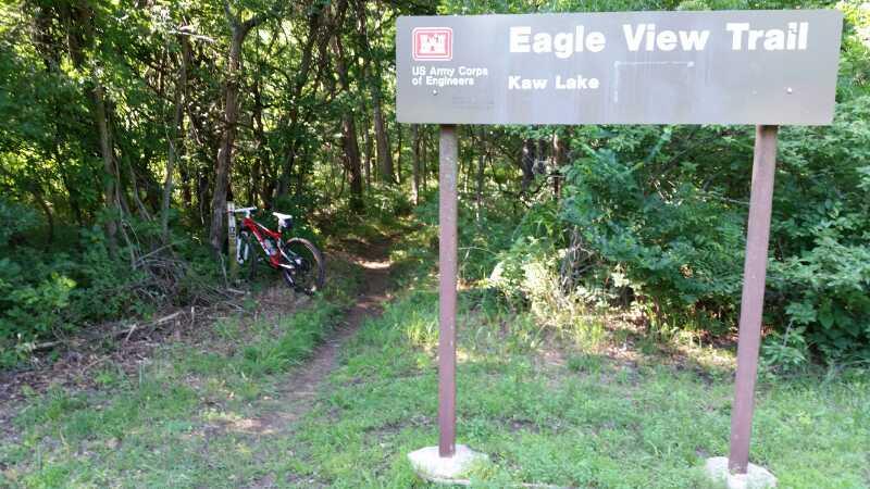 A trail sign for the Eagle View Trail at Kaw Lake, surrounded by lush greenery, with a bicycle parked beside it. Eagle View, Kaw Lake mountain bike trail.