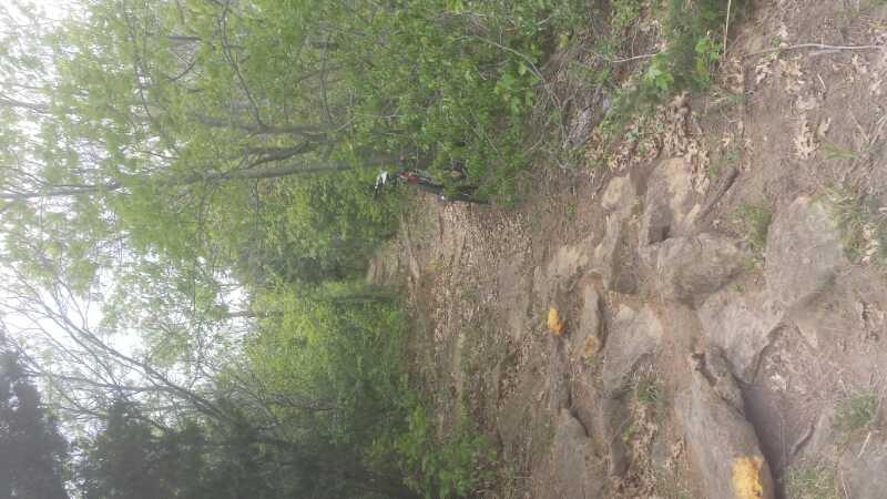 A rocky hiking trail surrounded by lush green trees and vegetation, with a bicycle resting against a tree in the background. Eagle View, Kaw Lake mountain bike trail.